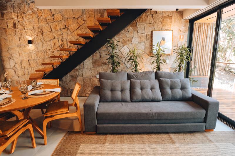 Sala do bangalô Abraço com parede de pedra, escada e a mata na janela
