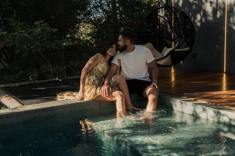Casal sentado na borda da piscina aquecida do bangalô Sorriso