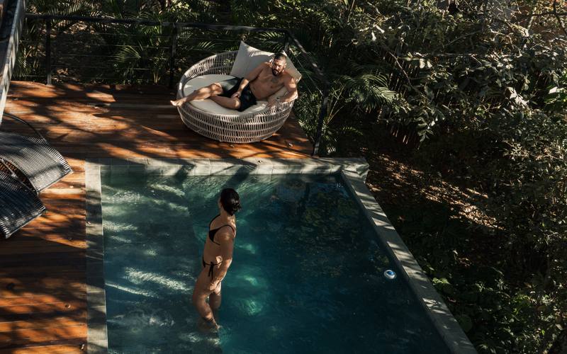 Piscina privativa do bangalô Sorriso com o daybed no deck, cercada pela mata